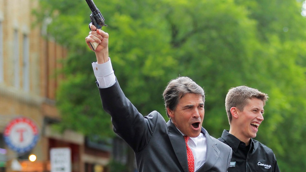 Texas Republican Gov. Rick Perry fires a six shooter filled with blanks as NASCAR driver Colin Braun looks on at an event in downtown Fort Worth, Texas on April 15, 2010.