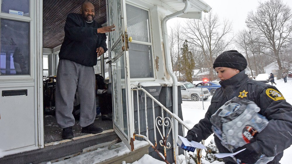 Samuel Smith receives a case of bottled water and a new water filter in Flint, Mich., as volunteers, Michigan State Police and Gennessee County Sheriff's Deputies deliver to residents, Jan 12, 2016. (Photo by Dale G. Young/The Detroit News/AP)