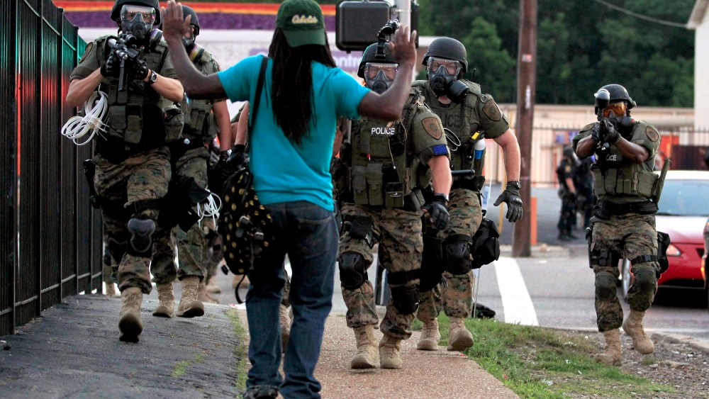 In this Aug. 11, 2014 file photo, police wearing riot gear walk toward a man with his hands raised in Ferguson, Mo. (Photo by Jeff Roberson/AP)