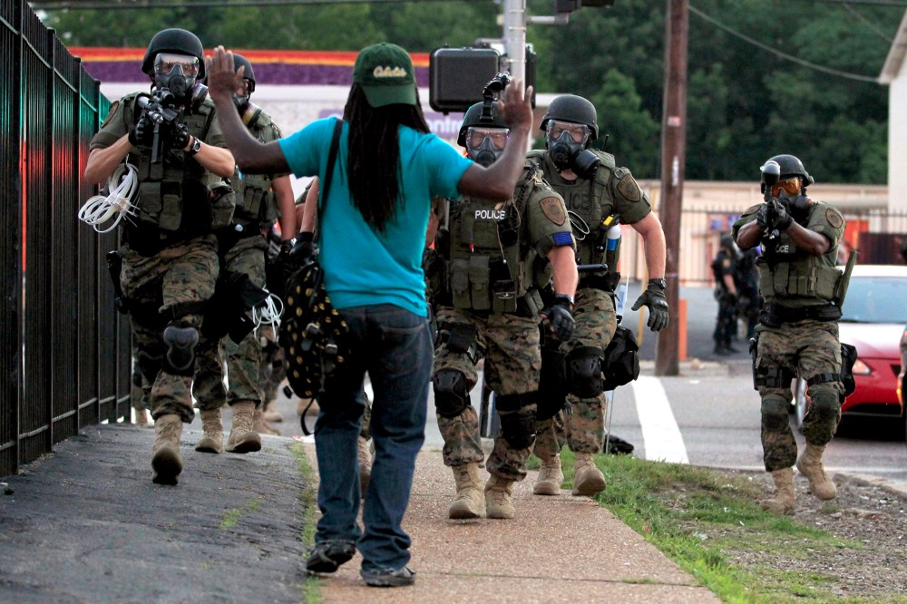 In this Aug. 11, 2014 file photo, police wearing riot gear walk toward a man with his hands raised in Ferguson, Mo. (Photo by Jeff Roberson/AP)