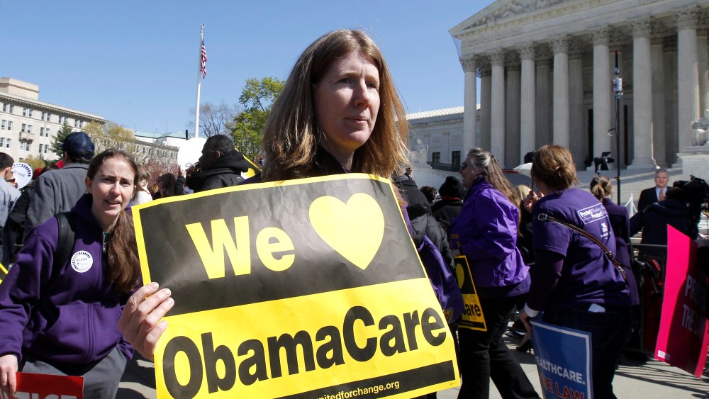 File Photo: Holding a sign saying "We Love ObamaCare" supporters of health care reform rally in front of the Supreme Court in Washington, Tuesday, March 27, 2012, as the court continued hearing arguments on the health care law signed by President...