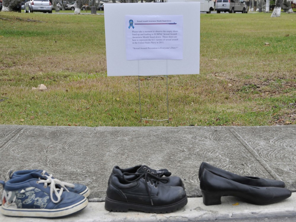 A Friday April 6, 2012 photo provided by the US Navy shows a sign that is displayed describing the 611 pairs of shoes lining the sidewalk in front of Sharkey Theater before a sexual assault event at Joint Base Pearl Harbor-Hickam in Hawaii. The shoes...