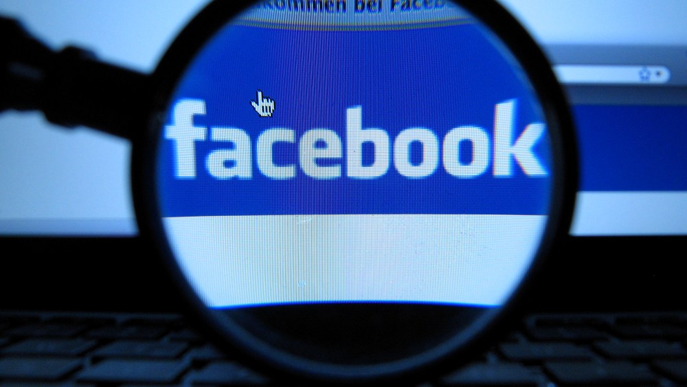 A magnifying glass is posed over a monitor displaying a Facebook page in Munich on Oct. 10, 2011. (Photo by Joerg Koch/AP)
