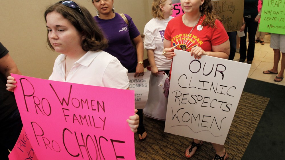 Protesters hold signs as they arrive for the start of a State Board of Health meeting in Richmond, Va.,  on June 15, 2012.