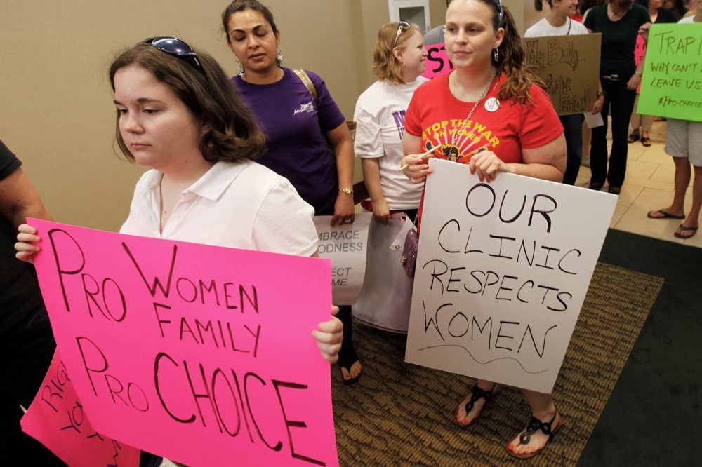 Protesters hold signs as they arrive for the start of a State Board of Health meeting in Richmond, Va., on June 15, 2012.