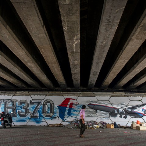 A man walks past MH370 related street art under a flyover in Kuala Lumpur, Malaysia on March 6, 2015. (Photo by Joshua Paul/AP)