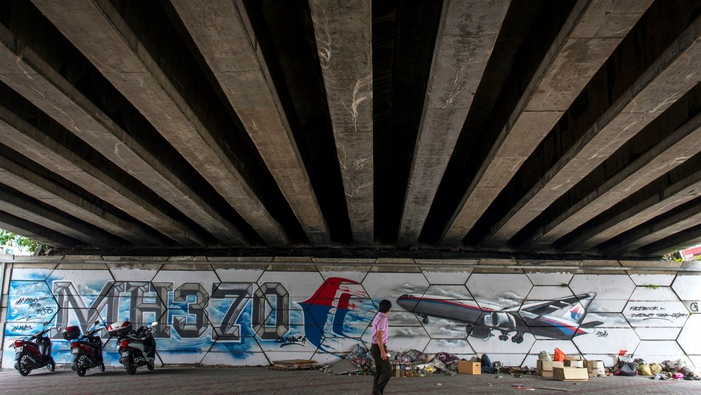 A man walks past MH370 related street art under a flyover in Kuala Lumpur, Malaysia on March 6, 2015. (Photo by Joshua Paul/AP)
