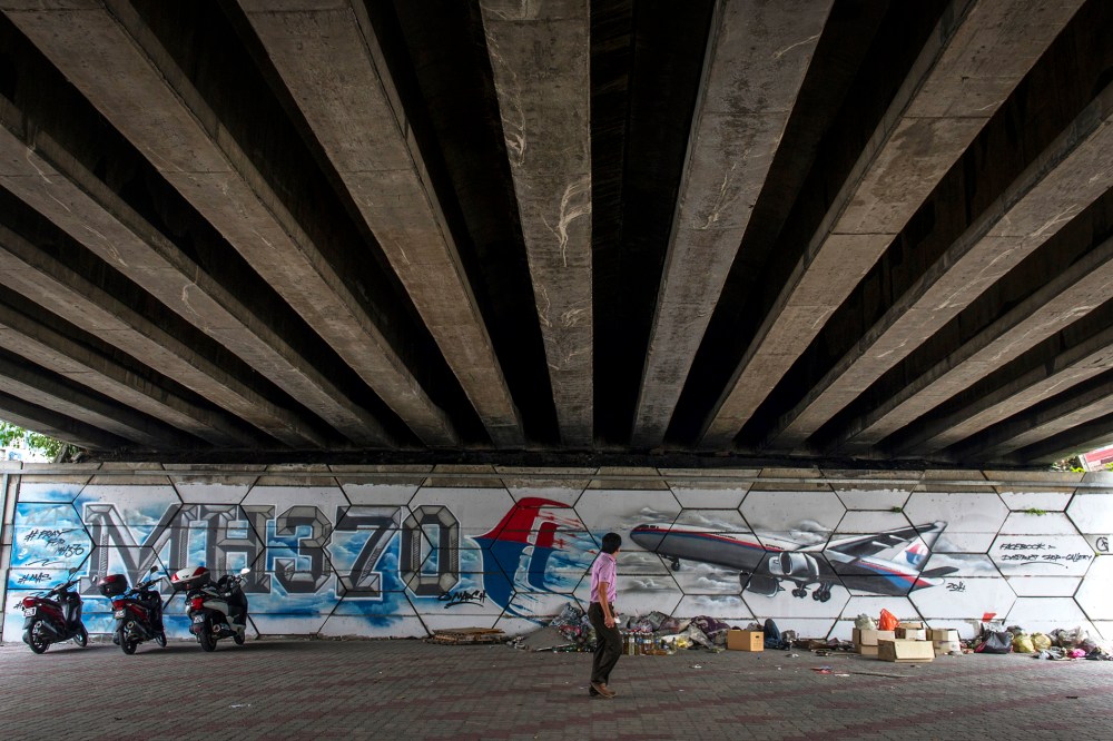 A man walks past MH370 related street art under a flyover in Kuala Lumpur, Malaysia on March 6, 2015. (Photo by Joshua Paul/AP)