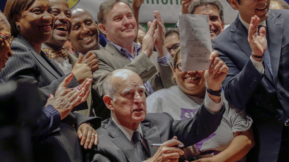 California Gov. Jerry Brown lifts a signed bill creating highest statewide minimum wage at $15 an hour by 2022 at the Ronald Reagan building in Los Angeles,April 4, 2016. (Photo by Nick Ut/AP)