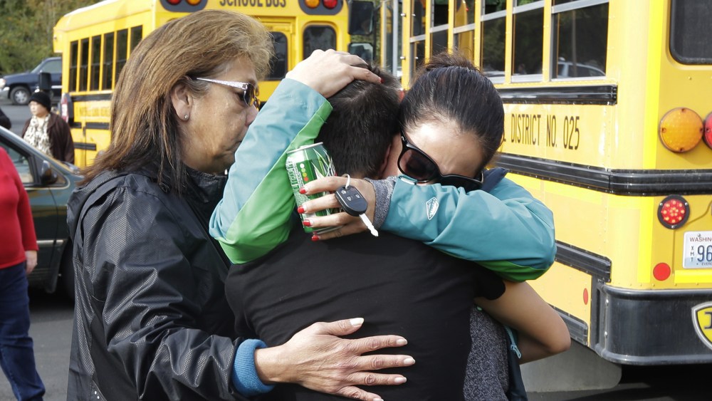 People embrace in front of school busses at a church, Oct. 24, 2014, where students were taken to be reunited with parents following a shooting at Marysville Pilchuck High School in Marysville, Wash. (Photo by Ted S. Warren/AP)