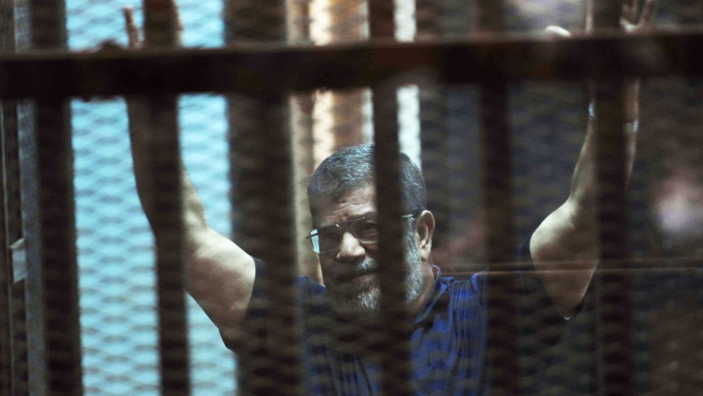 Ousted Egyptian President Mohammed Morsi raises his hands as he sits behind glass in a courtroom in Egypt on May 16, 2015. (Photo by Ahmed Omar/AP)