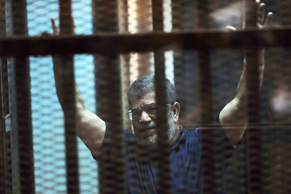 Ousted Egyptian President Mohammed Morsi raises his hands as he sits behind glass in a courtroom in Egypt on May 16, 2015. (Photo by Ahmed Omar/AP)
