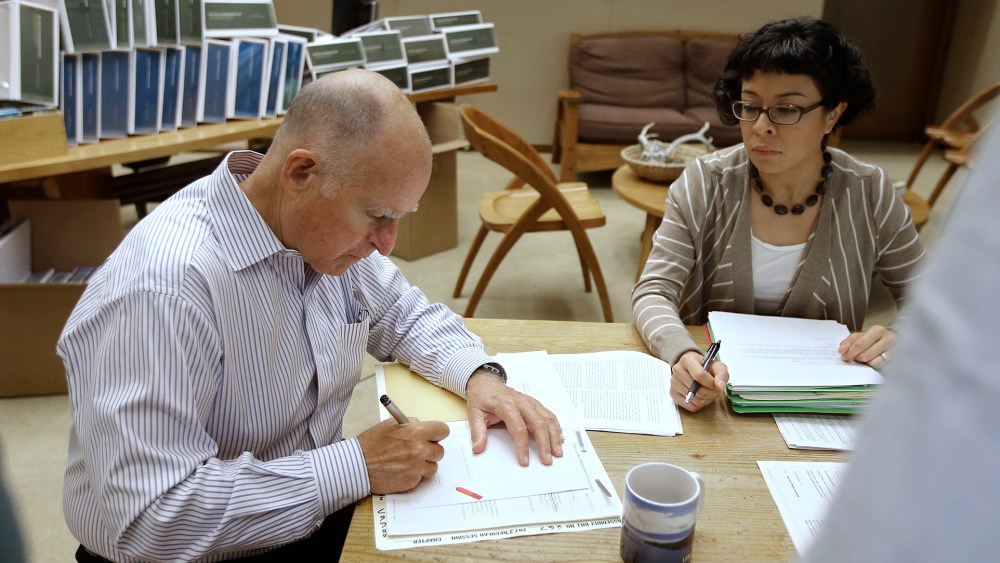 California Gov. Jerry Brown signs one of the hundreds of bills he has left to deal with as Garciela Castillo-Krings, his deputy legislative secretary, looks on at his Capitol office in Sacramento, Calif., Oct. 9, 2015. (Photo by Rich Pedroncelli/AP)