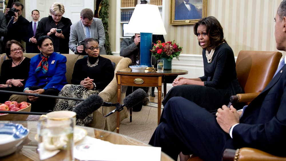 First Lady Michelle Obama speaks to the media as President Barack Obama listens as they meet with a group of mothers in the Oval Office of the White House in Washington, Dec. 18, 2013.