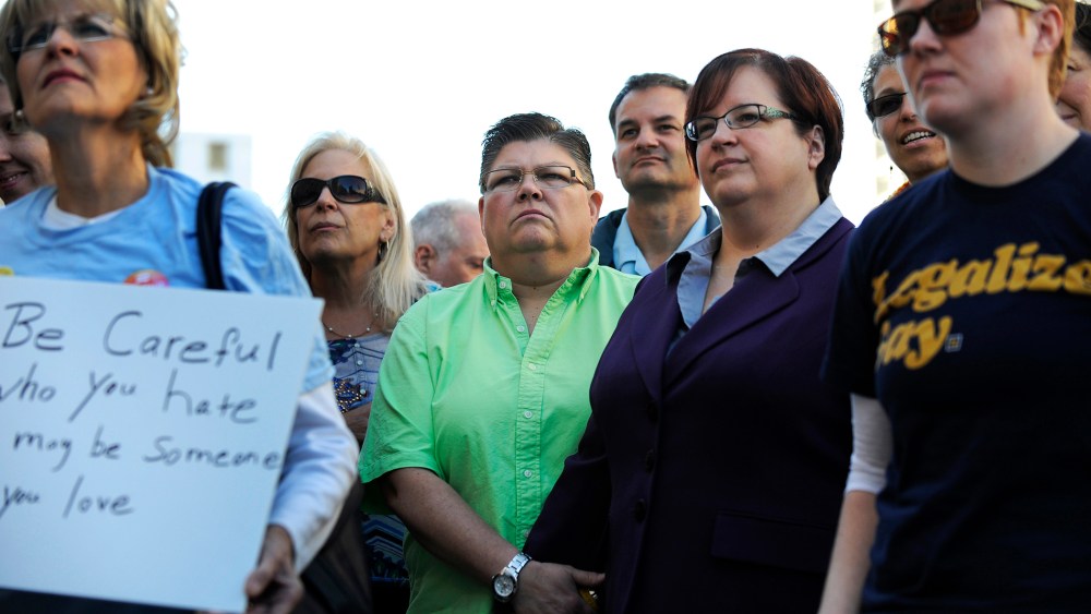 Same sex couple Jayne Rowse , green shirt, and April DeBoer hold hands during the rally outside the federal courthouse, Oct. 12, 2013, in Detroit, Mich.