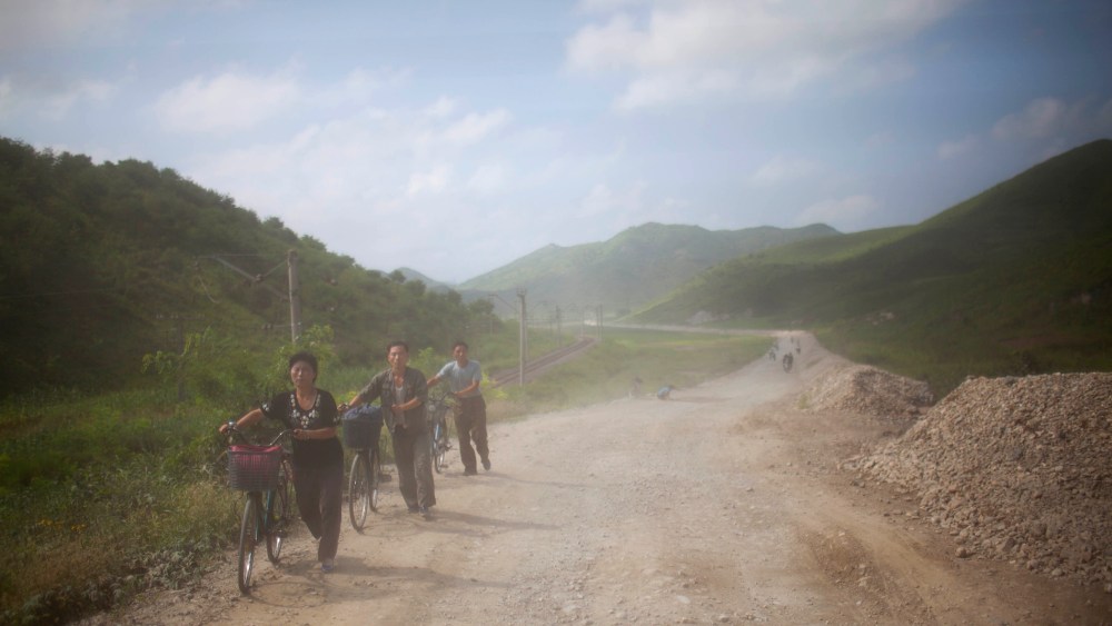 North Koreans are dusted by passing vehicles as they push their bicycles down a dirt road in Songchon County, North Korea on Aug 13, 2012.