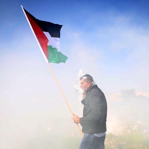 A Palestinian protester wearing a plastic bag on his face, waves a Palestinian flag among tear gas fired by Israeli security forces during clashes following a demonstration against Jewish settlements in the West Bank village of Bilin, west of Ramallah.