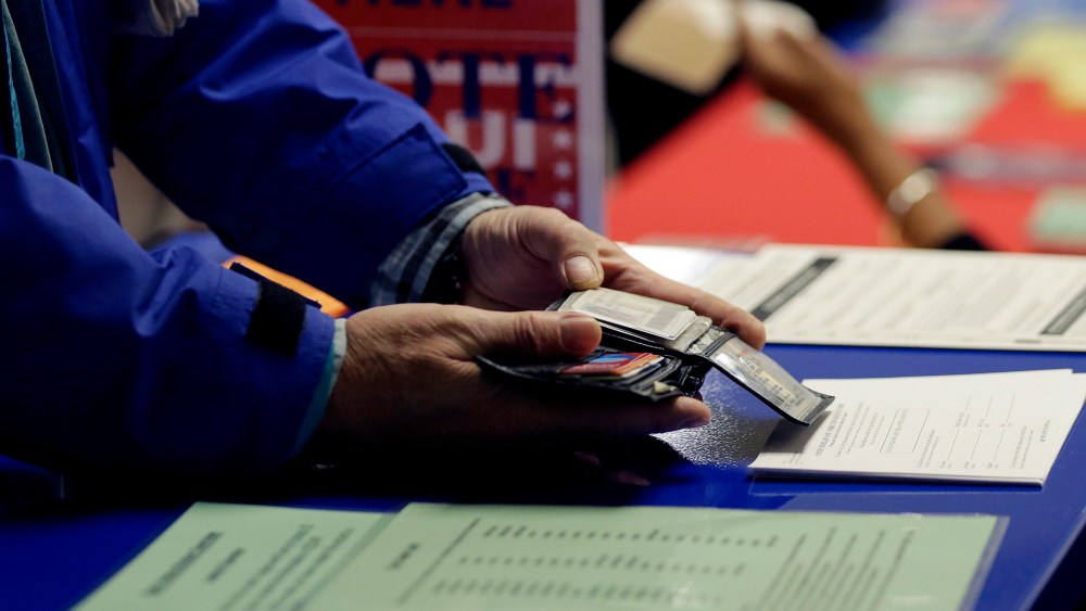 A voter shows his photo identification to an election official at an early voting polling site, in Austin, Texas on Feb. 26, 2014.