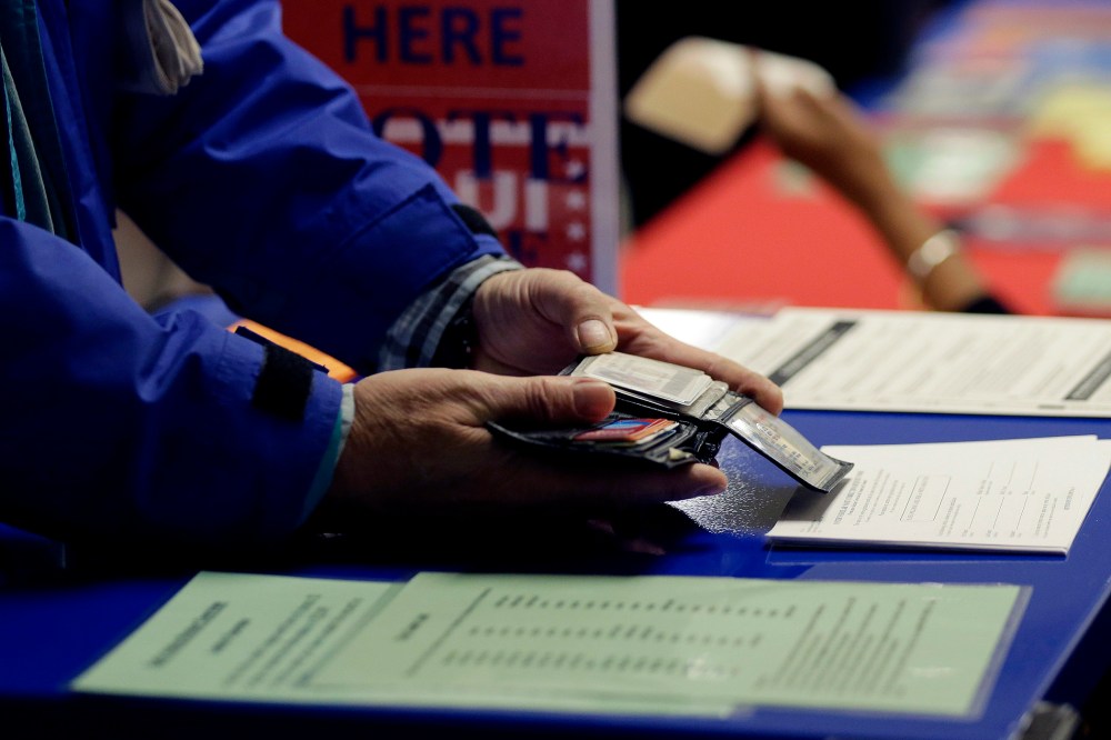 A voter shows his photo identification to an election official at an early voting polling site, Feb. 26, 2014, in Austin, Texas.