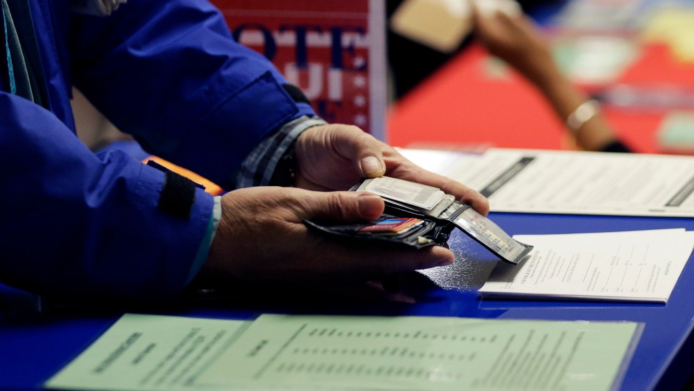 A voter shows his photo identification to an election official at an early voting polling site, in Austin, Texas on Feb. 26, 2014.