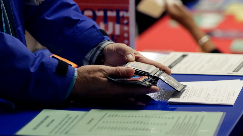 A voter shows his photo identification to an election official at an early voting polling site, in Austin, Texas, Feb. 26, 2014. (Photo by Eric Gay/AP)