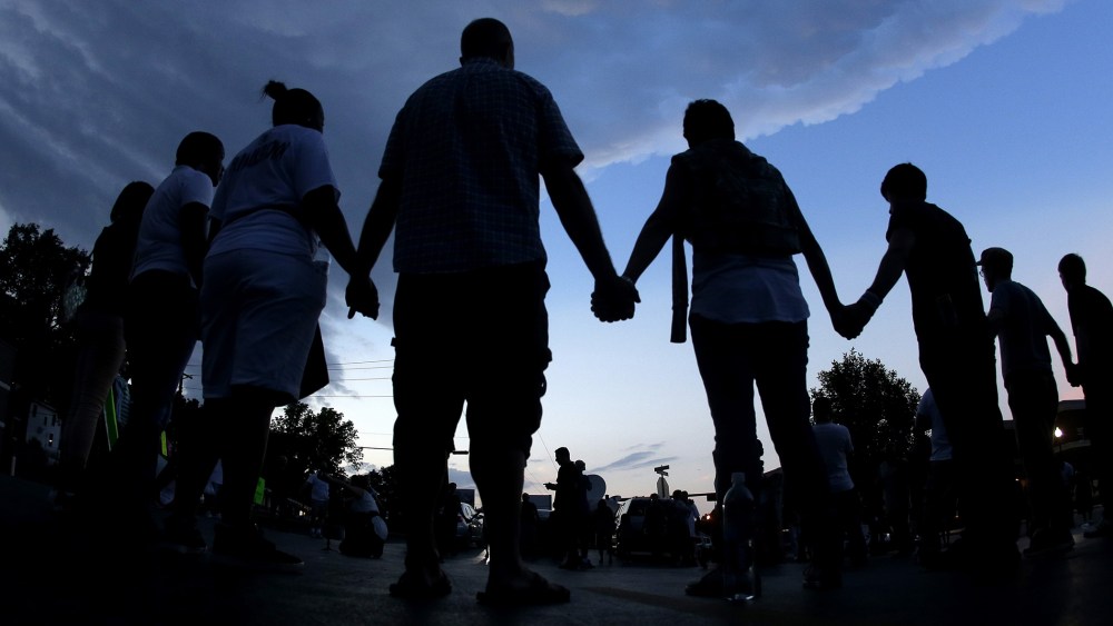 In this Aug. 20, 2014 fill photo people stand in prayer after march in Ferguson, Mo., to protest the shooting of Michael Brown. (Photo by Charlie Riedel/AP)