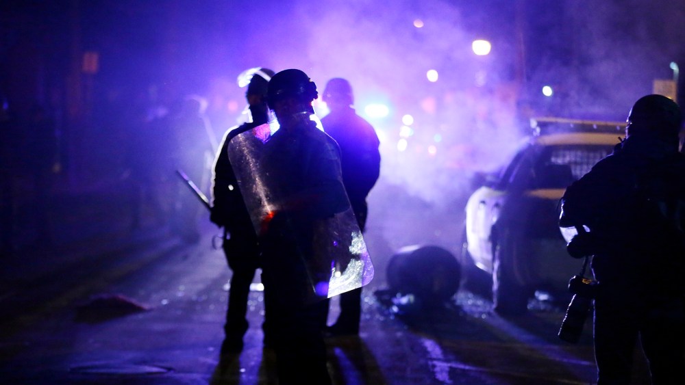 In this Nov. 25, 2014 file photo, police officers watch protesters as smoke fills the streets in Ferguson, Mo. after a grand jury's decision in the fatal shooting of Michael Brown. (Photo by Charlie Riedel/AP)