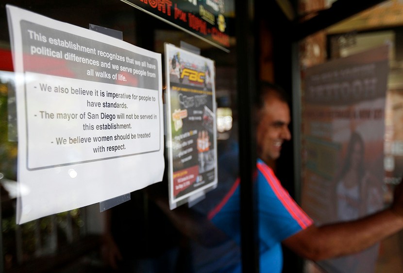 A man passes a sign, left,  posted on the outside of the entrance to a Hooters restaurant stating that San Diego Mayor Bob Filner will not be served Tuesday, Aug. 13, 2013, in San Diego. (Photo by Gregory Bull/AP)