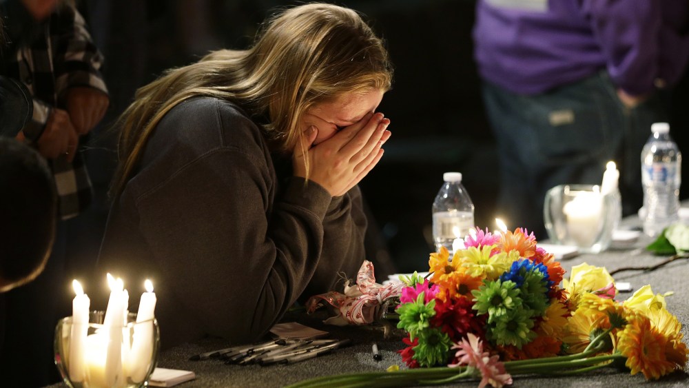 A young woman holds her head in her hands as she kneels before candles and flowers placed on the stage at the Grove Church in Marysville, Wash., Oct. 24, 2014, after a memorial vigil held for people affected by a shooting at Marysville Pilchuck High Schoo
