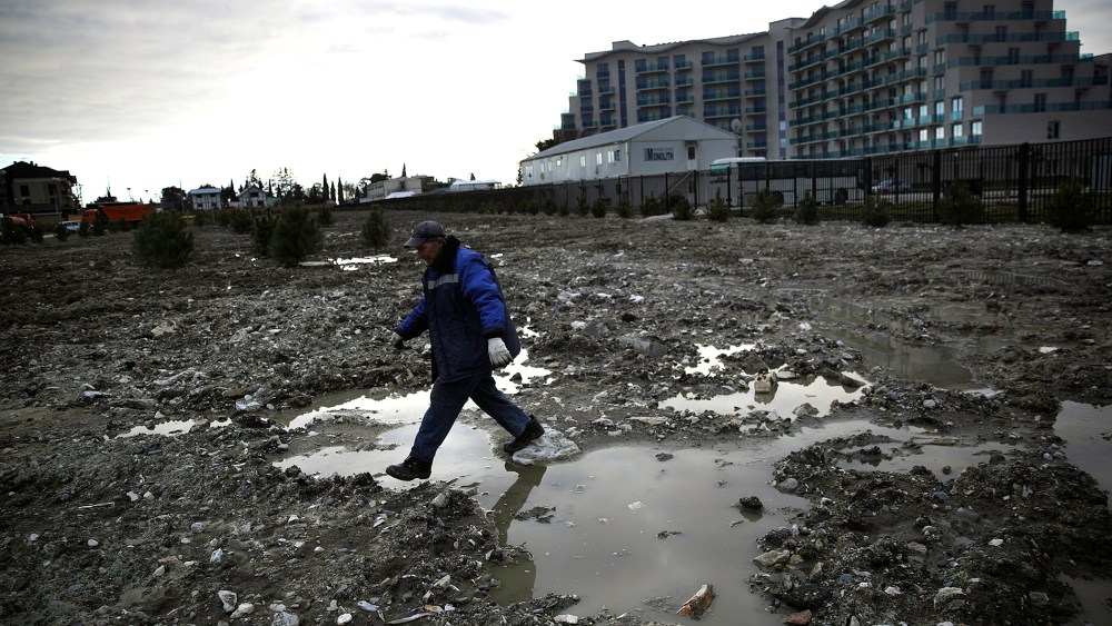 A construction worker steps over a puddle in a lot being prepared to be turned into a grassy lawn on Feb. 6, 2014, in Sochi, Russia.