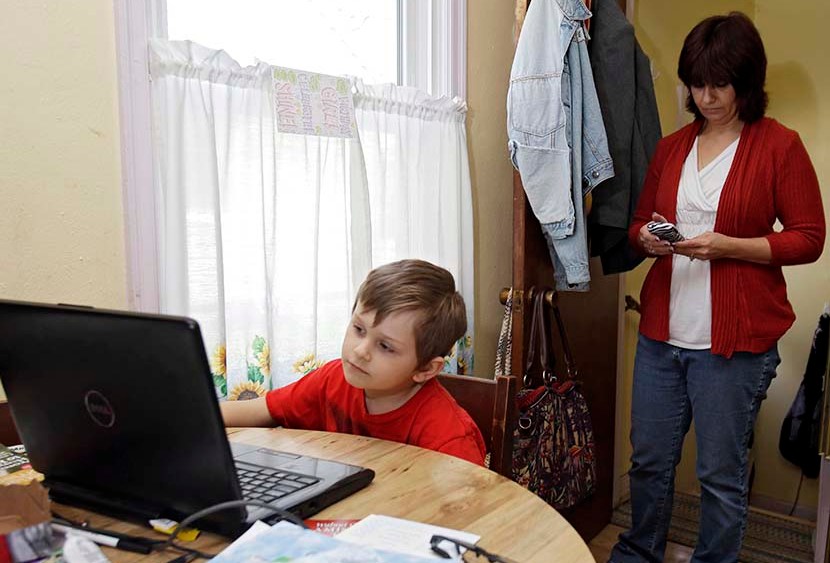 Larissa Bukowski, right, checks messages as her son David, 6, works on an online lesson in their home in Akron, Ohio. (Photo by Mark Duncan/AP)