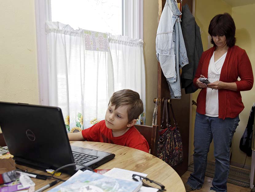 Larissa Bukowski, right, checks messages as her son David, 6, works on an online lesson in their home in Akron, Ohio. (Photo by Mark Duncan/AP)