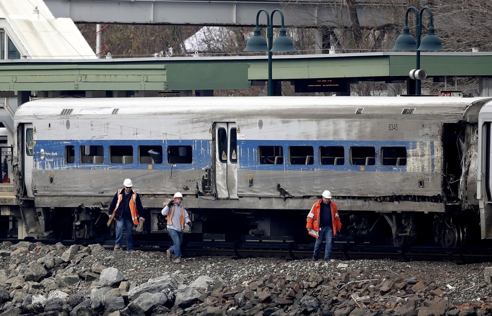 Workers walk past a Metro-North train car that was damaged in a derailment in the Bronx section of New York, Dec. 2, 2013.