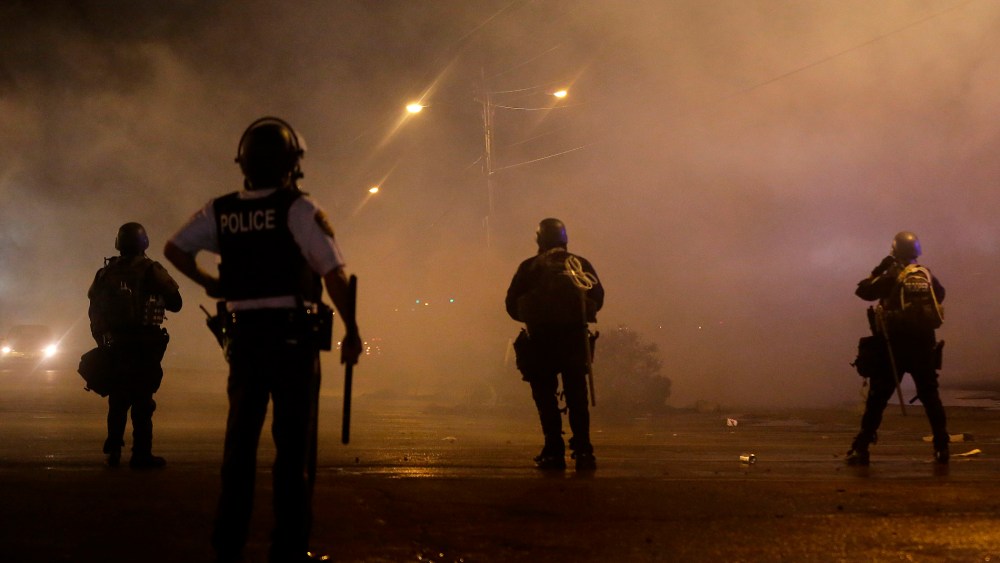 A law enforcement officer watches Sunday, Aug. 17, 2014, as tear gas is fired to disperse a crowd protesting the shooting of teenager Michael Brown last Saturday in Ferguson, Mo.