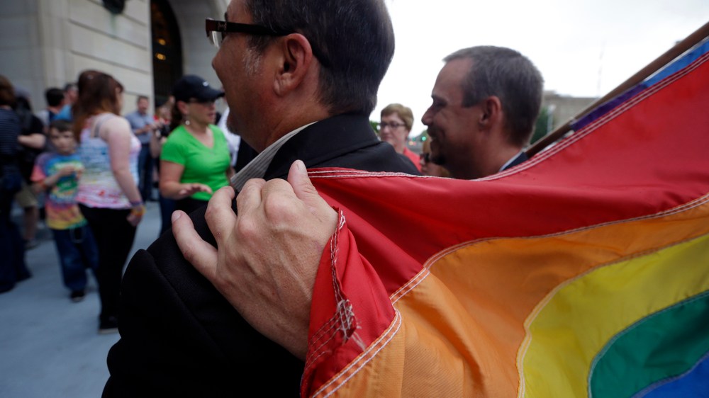 Shon DeArmon, right, puts his arm around his partner James Porter while holding a flag outside the Pulaski County Courthouse in Little Rock, Ark., May 12, 2014.