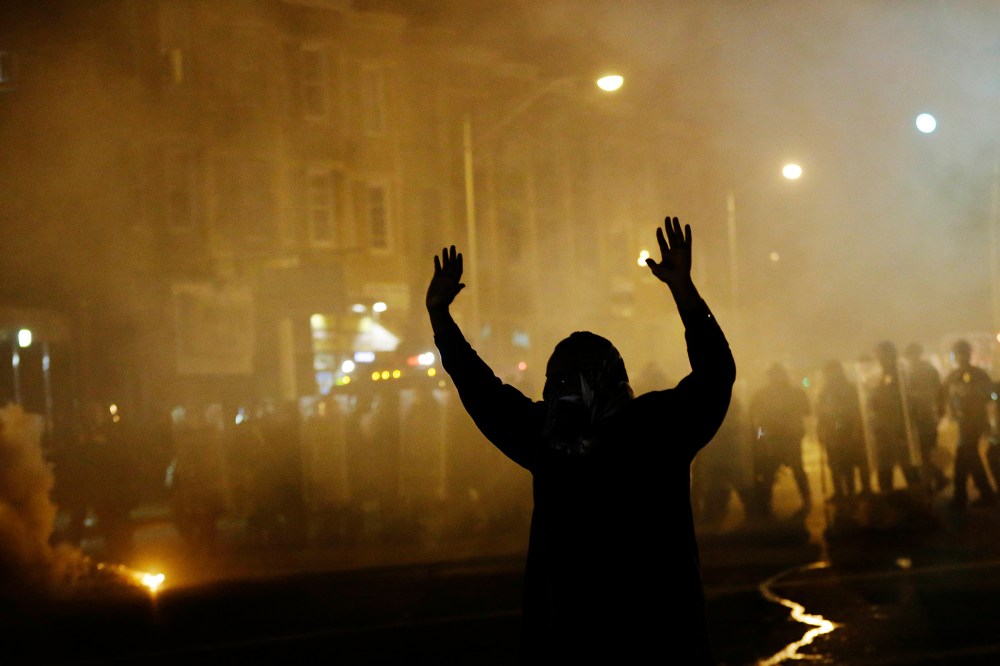 A protestor walks away as police in riot gear advance on the crowd after a 10 p.m. curfew went into effect in the wake of Monday's riots following the funeral for Freddie Gray, April 28, 2015, in Baltimore. (Photo by David Goldman/AP)