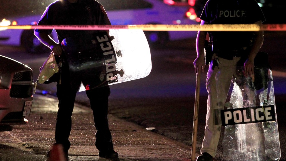 Police wearing riot gear stand at a post as they wait for a crowd to disperse, Aug. 11, 2014, in Ferguson, Mo.