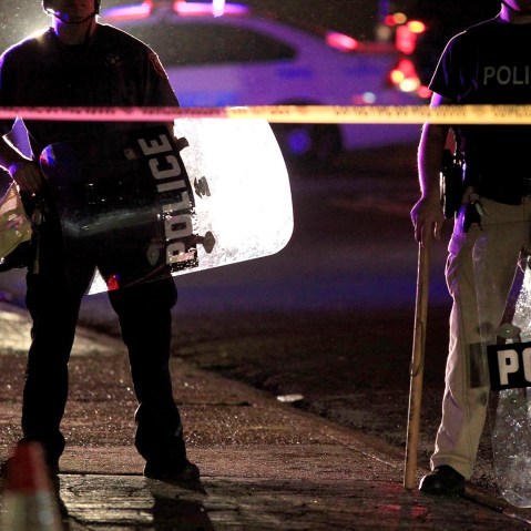 Police wearing riot gear stand at a post as they wait for a crowd to disperse Monday, Aug. 11, 2014, in Ferguson, Mo.