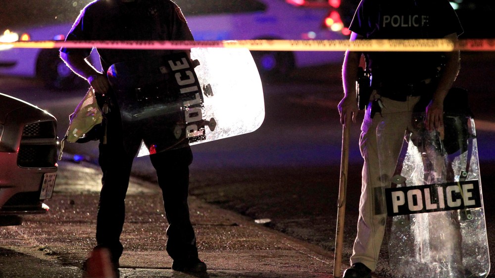 Police wearing riot gear stand at a post as they wait for a crowd to disperse Monday, Aug. 11, 2014, in Ferguson, Mo.