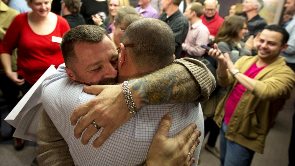 Chris Serrano, left, and Clifton Webb embrace after being married, as people wait in line to get licenses outside of the marriage division of the Salt Lake County Clerk's Office in Salt Lake City, Dec. 20, 2013.
