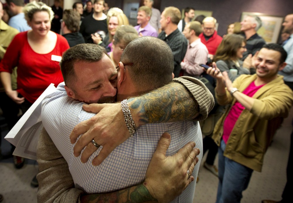 Chris Serrano, left, and Clifton Webb embrace after being married, as people wait in line to get licenses outside of the marriage division of the Salt Lake County Clerk's Office in Salt Lake City, Dec. 20, 2013.
