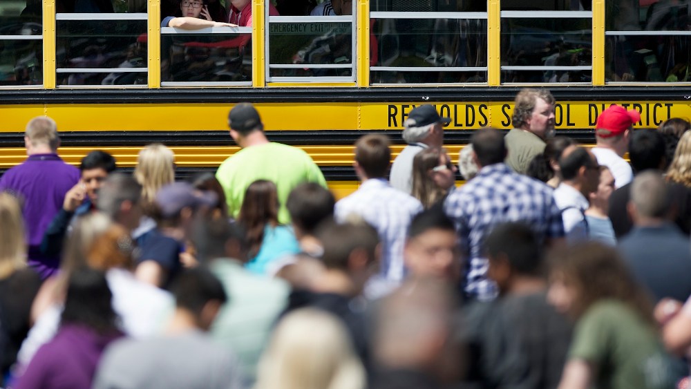 Students try to communicate and locate their family while waiting on a school bus as they arrived at a shopping center parking lot in Wood Village, Ore., after a shooting at Reynolds High School, June 10, 2014.