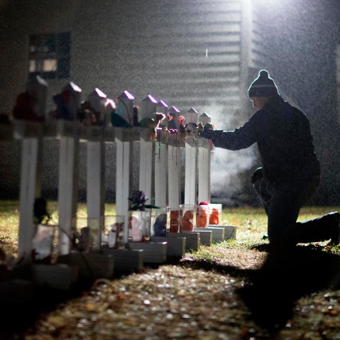 A man adjusts a display of wooden crosses, and a Jewish Star of David, representing the victims of the Sandy Hook Elementary School shooting, on his front lawn, Dec. 17, 2012, in Newtown, Conn. (Photo by David Goldman/AP)