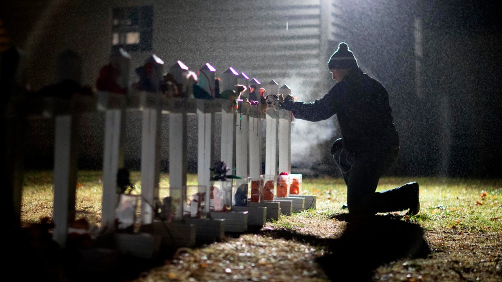 A man adjusts a display of wooden crosses, and a Jewish Star of David, representing the victims of the Sandy Hook Elementary School shooting, on his front lawn, Dec. 17, 2012, in Newtown, Conn. (Photo by David Goldman/AP)