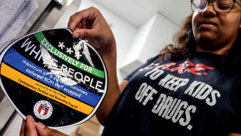 April Jensen, an employee at Sugar Mama's holds a sticker that the business found on the front of their store in Austin, Texas, March 18, 2015. (Photo by Austin American-Statesman, Rodolfo Gonzalez/AP)