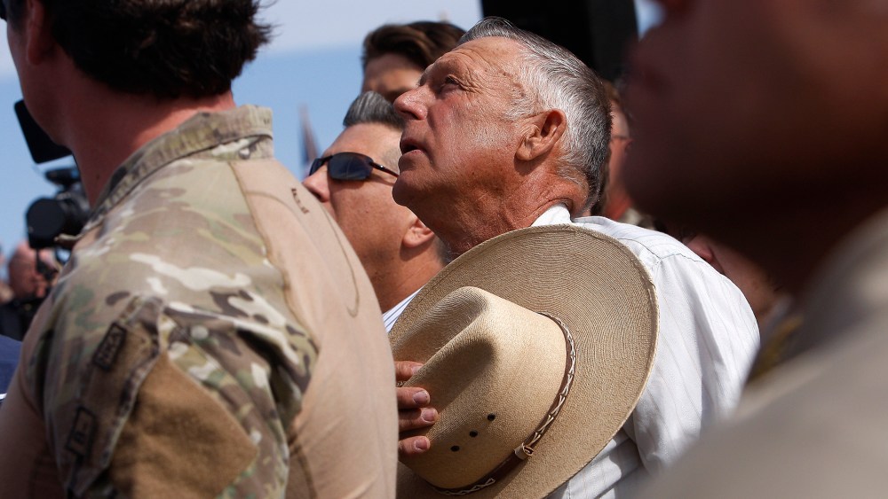 Surrounded by security personnel, rancher Cliven Bundy, middle, sings the National Anthem outside of Bunkerville while gathering with his supporters to challenge the BLM on April 12, 2014.