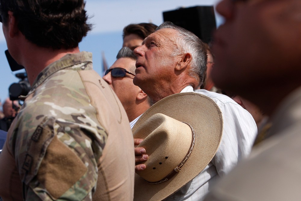 Surrounded by security personnel, rancher Cliven Bundy, middle, sings the National Anthem outside of Bunkerville while gathering with his supporters to challenge the BLM on April 12, 2014.