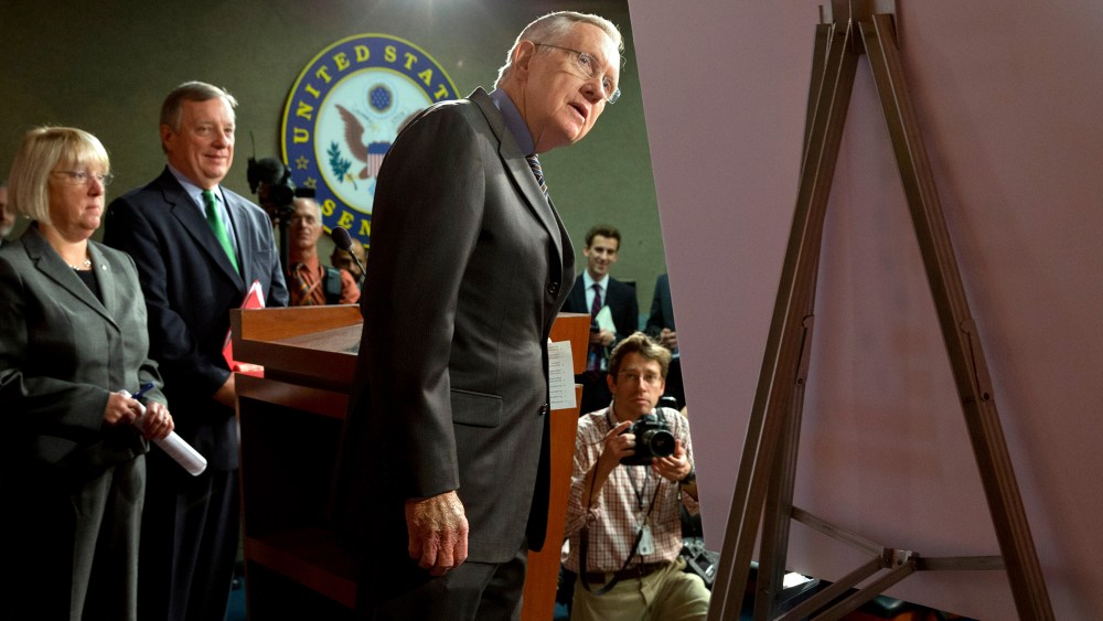 Senate Majority Leader Harry Reid of Nev., right, looks at a placard during a news conference in  Washington, on Nov. 21, 2013