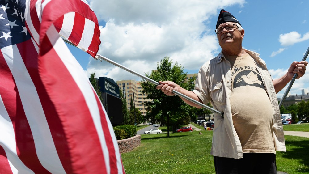 Dan Wilcox, of Albany holds flags in front of the Stratton VA Medical Center in Albany on Thursday, June 19, 2014, for a Veterans for Peace protest to demand adequate healthcare for veterans across the country.