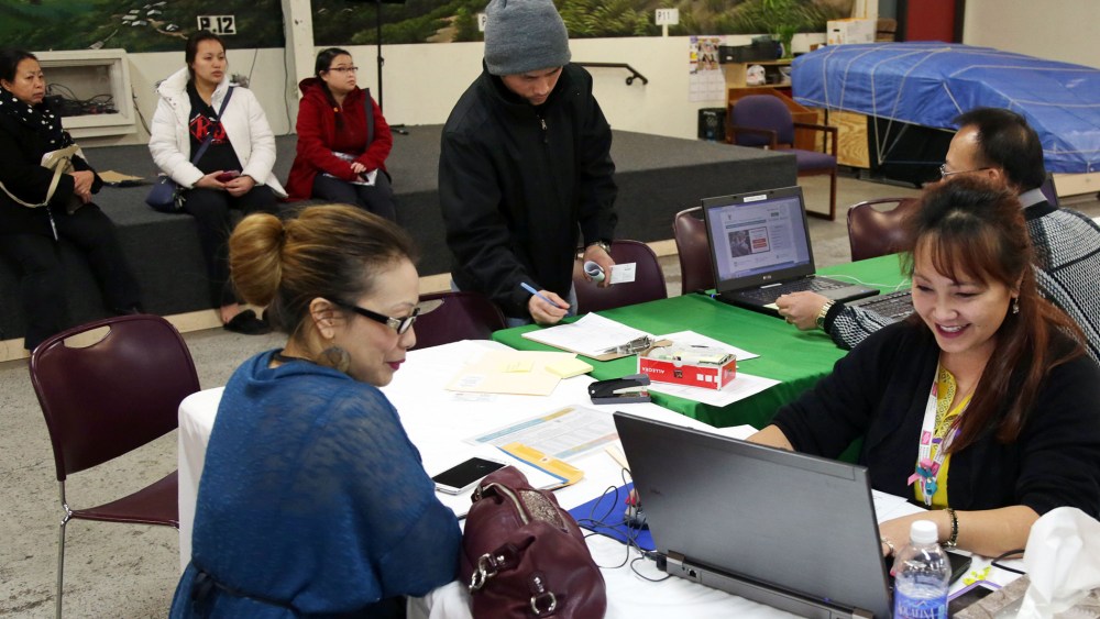 Mai Lo Lee, right, enrolls a woman in the state's insurance exchange, MNsure, as others (seated) from the Southeast Asian community wait their turn to register, on Feb. 13, 2015, in St. Paul, Minn. (Photo by Jim Mone/AP)